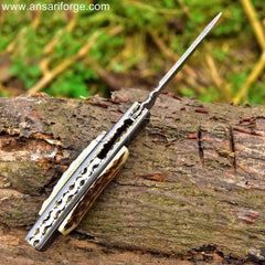 Custom Handmade Damascus steel pocket knife with raindrop pattern, stag antler handle, and leather sheath.