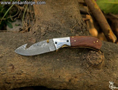 Open folding pocket knife with a 3.25-inch blade and gut hook, highlighting the beautiful layered pattern of the hand-forged Damascus steel.