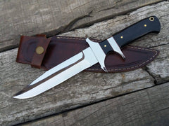 A close-up photo of the Loveless Knife, a beautiful hunting knife with a mirror-polished blade, stainless steel hilt and sub-hilt, and a buffalo horn handle. The knife rests in a rustic cowhide leather sheath.