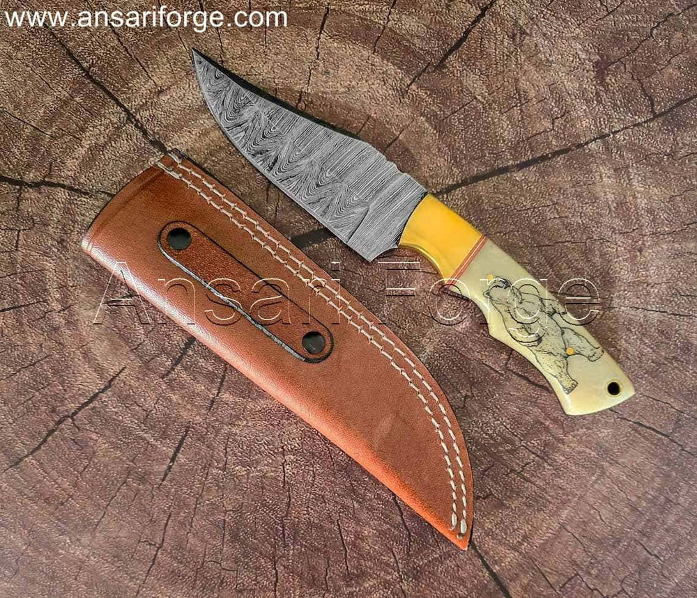 Hand-forged Damascus steel hunting knife with white camel bone handle, bear engraving, and leather sheath.