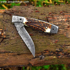 Hand-forged Damascus steel pocket knife with raindrop pattern, stag antler handle, and genuine leather sheath.