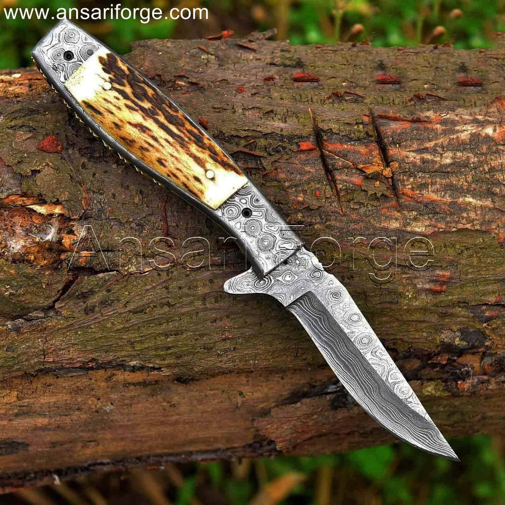Damascus steel pocket knife with raindrop pattern laying on woods, showcasing its sharp blade and comfortable grip.