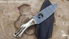Demascus knife with deer antler handle and handmade cowhide sheath on a wood background.