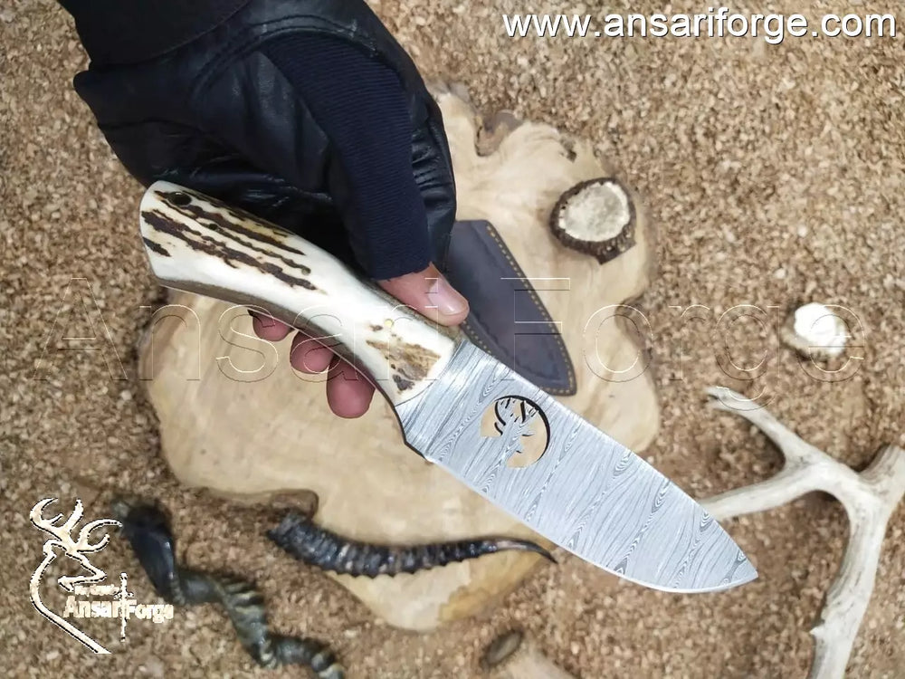 Demascus knife with deer antler handle and handmade cowhide sheath on a wood background.