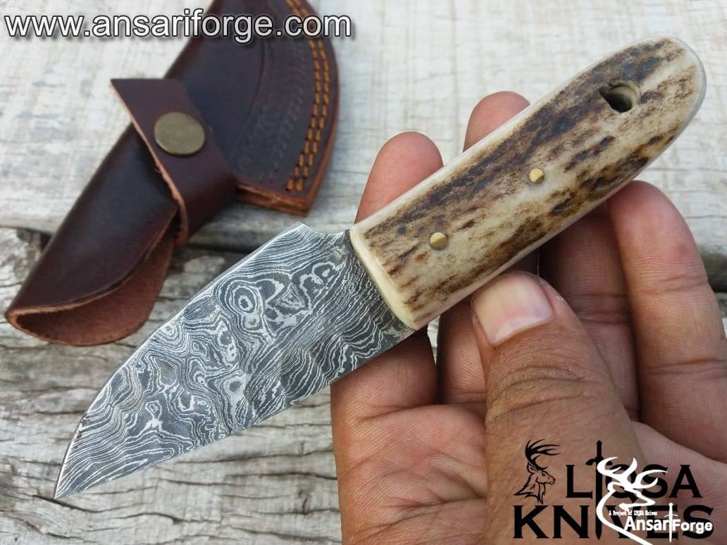 Stag Handle Damascus Knife with a hand-forged raindrop pattern blade, featuring a genuine sambar stag antler handle and a cowhide leather sheath, displayed on a rustic wooden background.