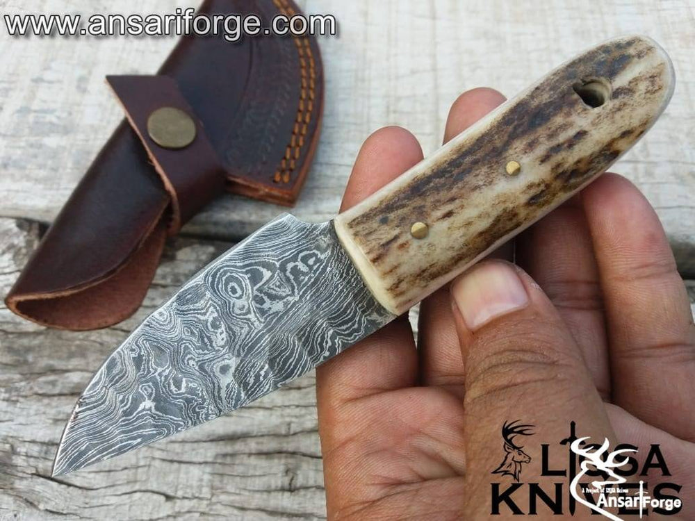 Stag Handle Damascus Knife with a hand-forged raindrop pattern blade, featuring a genuine sambar stag antler handle and a cowhide leather sheath, displayed on a rustic wooden background.