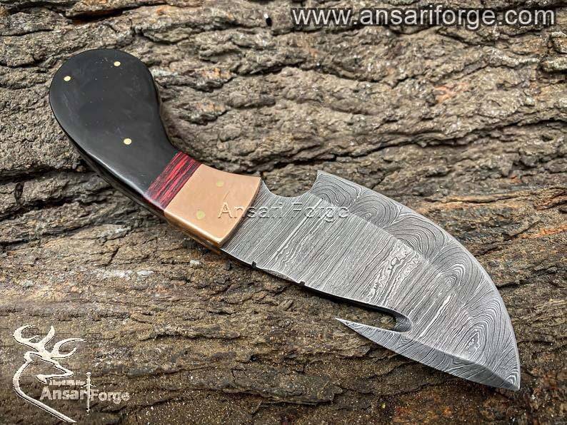 Hand forged Damascus steel gut hook skinning knife, showcasing intricate twist pattern and sharp blade.