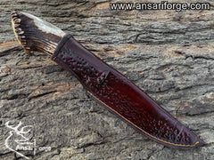 Custom made Damascus steel hunting knife with stag horn handle resting in handmade brown sheath, crafted from real cow skin leather.