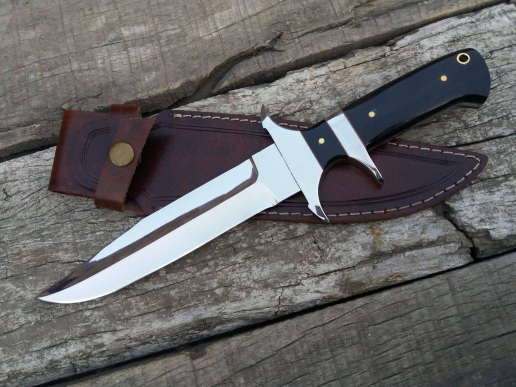 A close-up photo of the Loveless Knife, a beautiful hunting knife with a mirror-polished blade, stainless steel hilt and sub-hilt, and a buffalo horn handle. The knife rests in a rustic cowhide leather sheath.