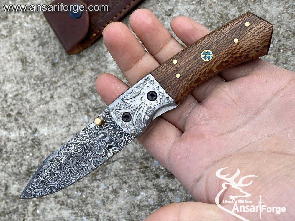 Close-up of a Damascus folding knife with blade open, showcasing the intricate layered pattern.