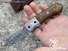 Close-up of a Damascus folding knife with blade open, showcasing the intricate layered pattern.